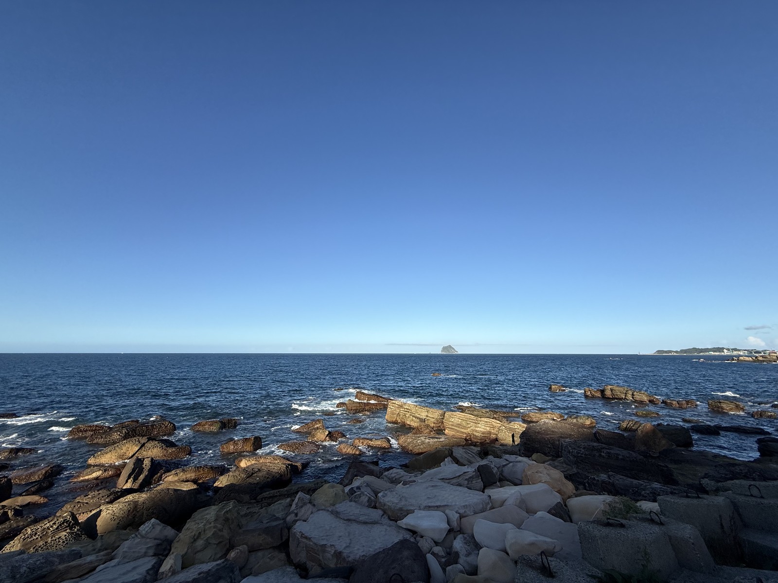 藍天下的海岸，海浪拍打前方的岩石。